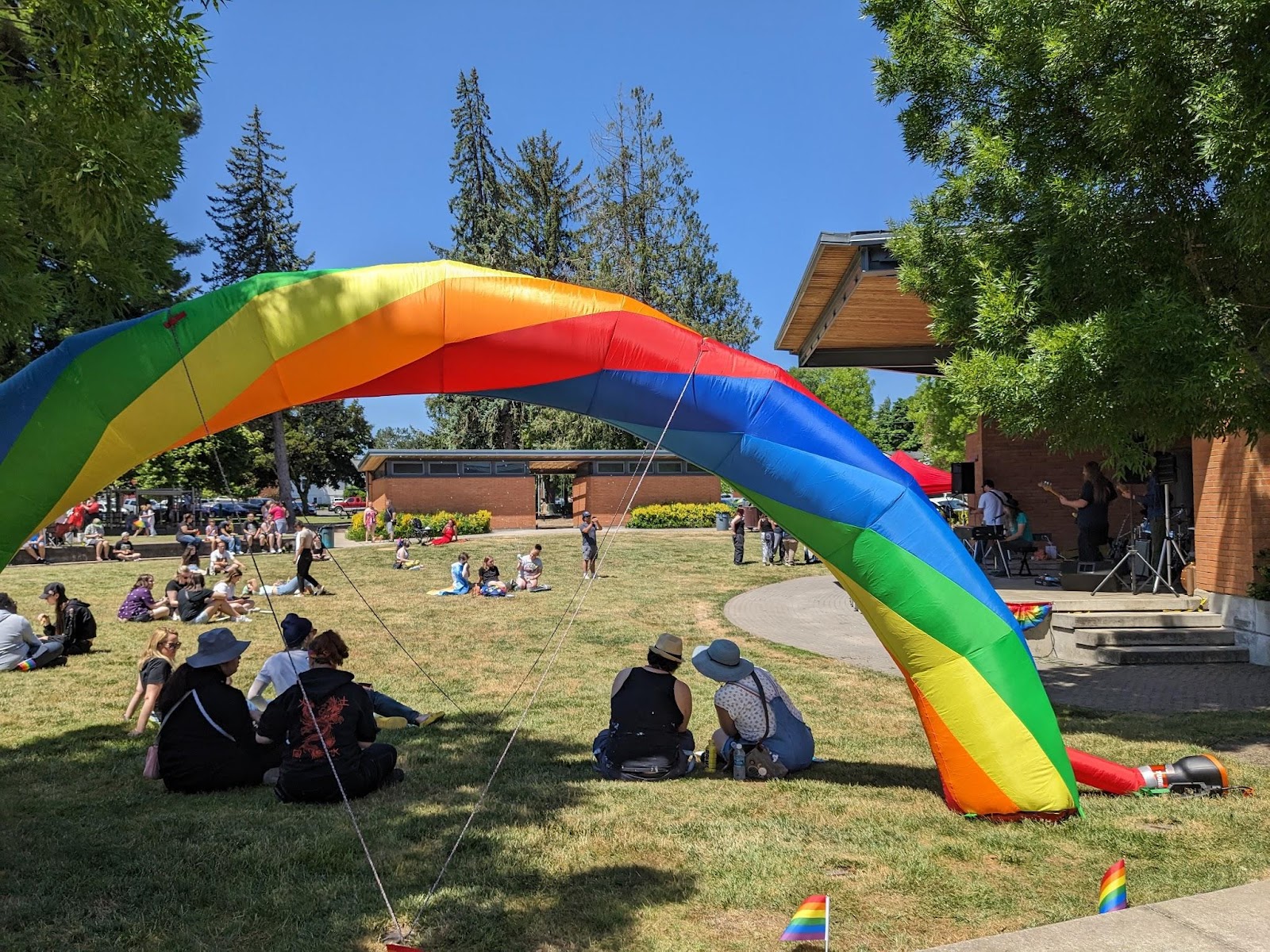 A photograph of a rainbow inflatable in Main Street park with people sitting in the grass enjoying the celebration