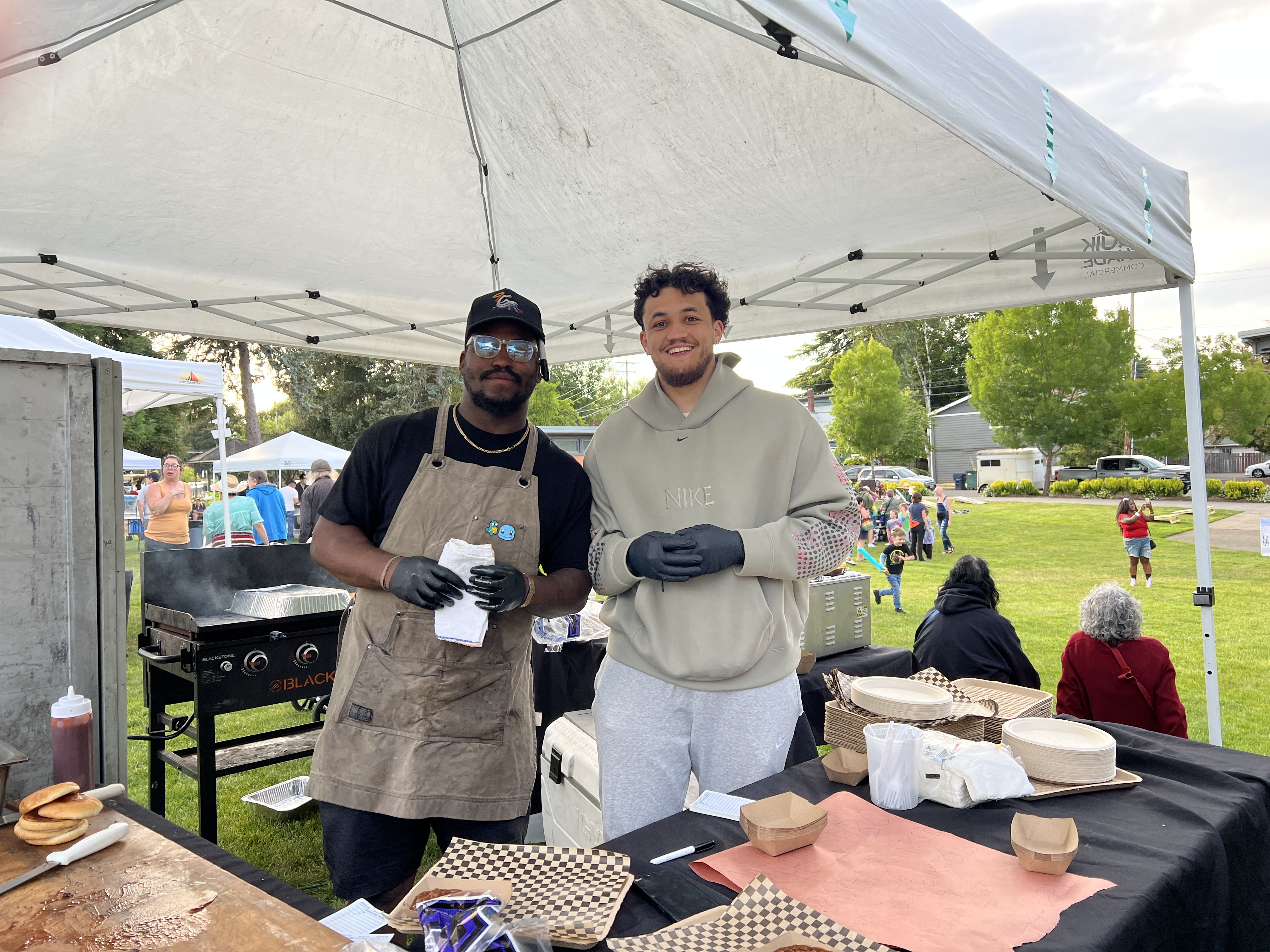 two gentlemen smiling and preparing barbeque for the Juneteenth celebration